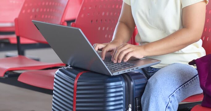 Woman working on a laptop placed on a suitcase while traveling, typing on laptop, remote work, digital nomad lifestyle, business travel, productivity, and flexible modern work