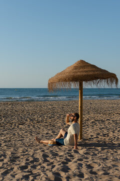 Vertical man relaxing under straw beach umbrella by the sea