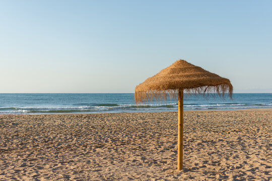 Straw beach umbrella on empty beach by the sea