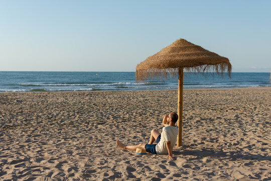 Man sitting under straw beach umbrella looking at the sea