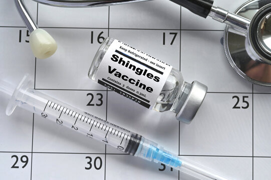 A medical syringe needle with vial of shingles vaccine laying on a calendar. Concept for scheduling immunization.