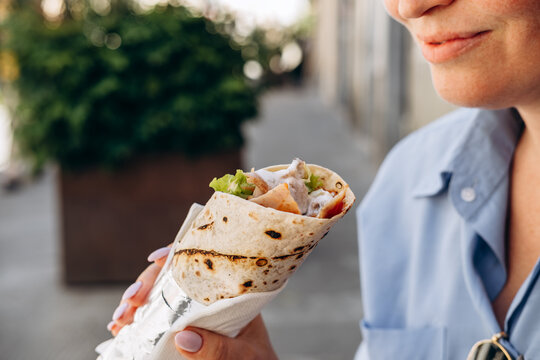 Woman Eating Burrito or Grilled Wrap Sandwich on City Street Enjoying Casual Outdoor Lunch Bite