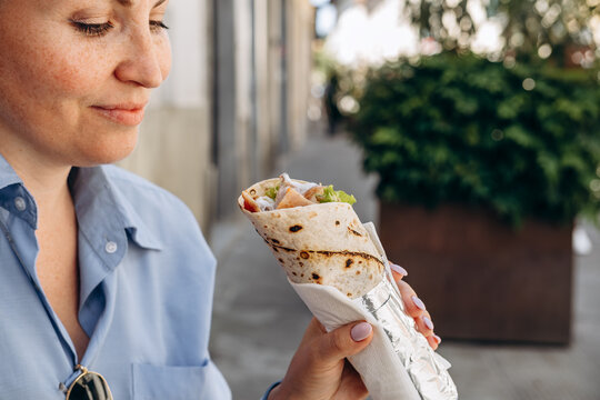 Woman Eating Burrito or Grilled Wrap Sandwich on City Street Enjoying Casual Outdoor Lunch Bite