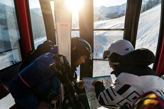 Scenic two skiers study trail map inside ski lift gondola at warm sunrise light at mountain alpine resort. Scenery group friends teamwork, planning, and excitement downhill winter sports adventure