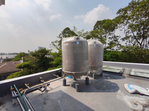 Two fiberglass material cylinder water storage tanks installed on a building concrete rooftop with PVC pipe installations.