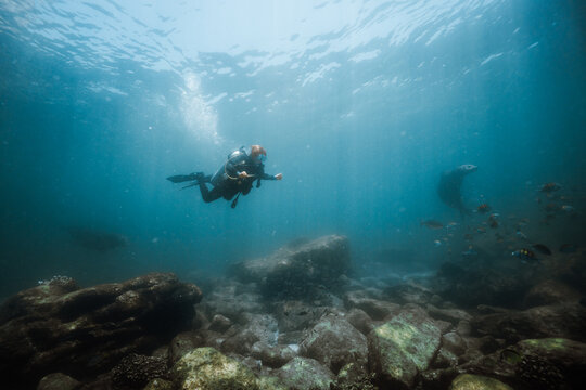 Young Scuba Diver Swimming Over Rocky Reef in Clear Blue Water w