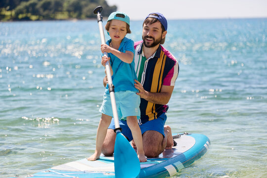 Father Teaching Son Paddle Boarding in Shallow Sea