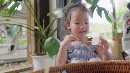 Fototapeta premium A focused young toddler girl expresses her creativity, carefully painting an art project with a brush to develop fine motor skills and enjoy learning at home.