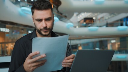 Serious focused Caucasian man businessman working with laptop and documents managing finance budget in business center male guy employer agent work with papers and computer cyberspace in shopping mall © Yuliia