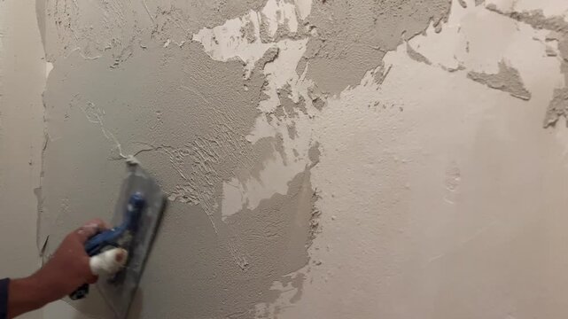 A person applies plaster to a drywall surface. The task takes place in a residential setting. Tools and plaster are used to create a smooth finish.