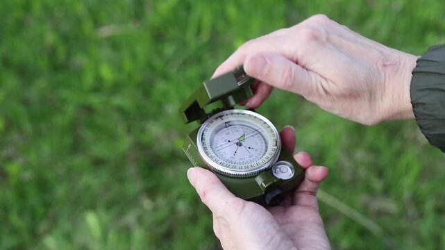 Hands of female traveler opening compass and using it to navigate in nature during summer hike.
