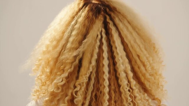 Slow motion intimate closeup of curly blonde hair moving and bouncing while subject turns head against neutral studio background