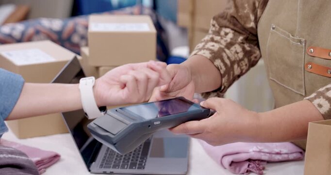 Retired asian woman small business uses POS terminal for smartwatch tap to pay, senior woman entrepreneur verifies invoice receipt, organizes handmade shibori fabric packaging, prepares delivery.