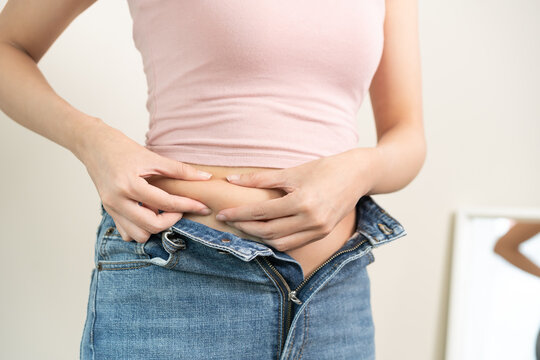 Weight gain, overweight, high cholesterol and pressure, woman hand pinching excess fat big belly with finger and wear tight trousers, show fat around abdomen body, getting loss, isolated on background