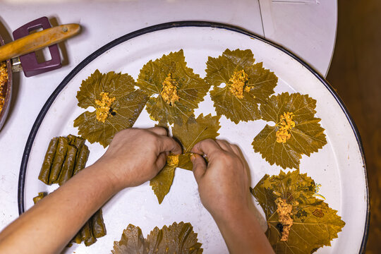 Close-up of hands placing seasoned rice filling onto preserved grape leaves while preparing homemade stuffed vine leaves. Traditional Turkish dolma cooking process.