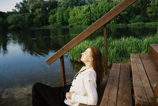 A woman rests beside a still lake framed by forest and reeds