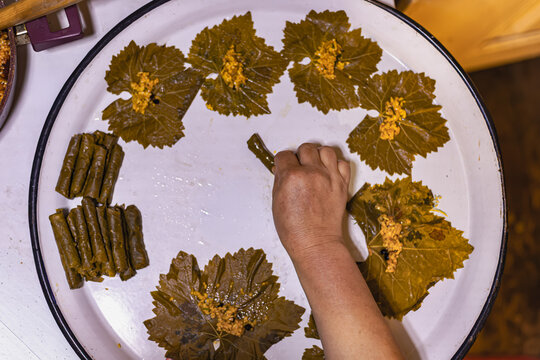 Close-up of hands placing seasoned rice filling onto preserved grape leaves while preparing homemade stuffed vine leaves. Traditional Turkish dolma cooking process.