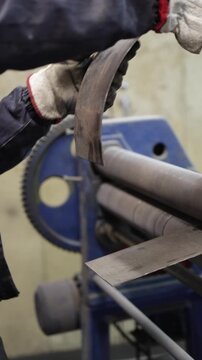 Close-up of a worker's hands in protective gloves using an industrial roller bending machine to shape a sheet of metal in a manufacturing plant workshop