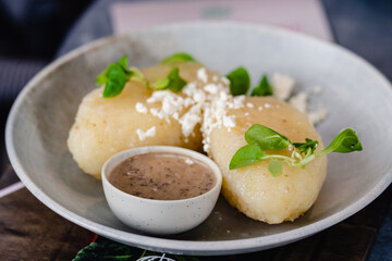 Vegan Cepelinai, a modern, plant-based adaptation of Lithuania’s national dish, which are large potato dumplings shaped like zeppelin airships,  presented on a ceramic plate in a restaurant © Michele Ursi