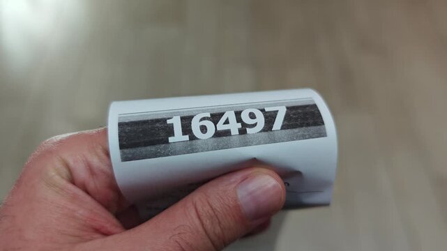 Close up of a man's hand holding a queue number ticket. Concept of waiting for service, managing customer flow, and patience