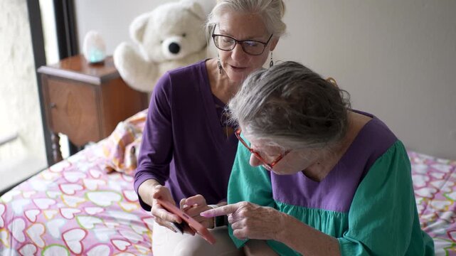 Mature daughter spends time with her elderly mother at a senior care facility sharing family photos and talking about their memories