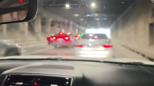 Driver's point of view sitting in a car slowly moving through a dimly lit city tunnel during a congested rush hour commute with blurry lights