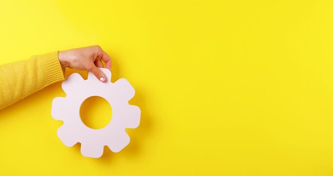 Close-up video of two hands holding rotating 3D gear symbols on a yellow background. Concept of settings, configuration, teamwork, engineering, automation, optimization, and technology.