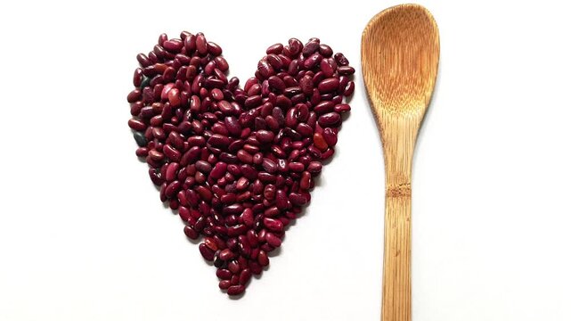 Studio shot of traditional raw dried red beans Phaseolus vulgaris arranged in a heart shape next to a vertical bamboo wooden spoon isolated on white background from Guatemala.