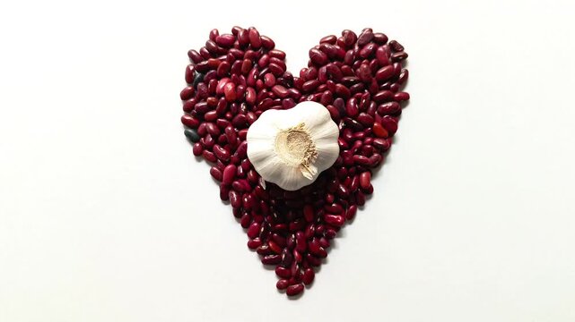 Studio shot of traditional raw dried red beans Phaseolus vulgaris arranged in a heart shape with a whole white garlic bulb Allium sativum in the center isolated on white background from Guatemala.