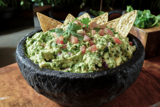 Guacamole dip in molcajete with tortilla chips and fresh herbs