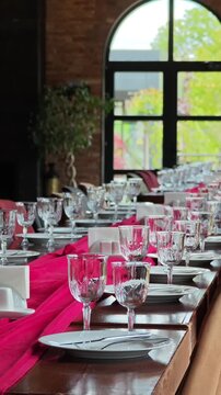 Long wooden table beautifully decorated for a formal dinner or wedding reception. Elegant glassware and cutlery ready for a festive event