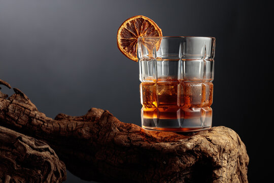 Old-fashioned cocktail with ice and a dried orange slice served on weathered driftwood.