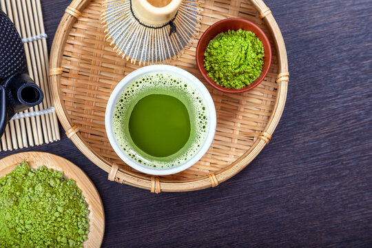 Bowl of matcha tea with bamboo whisk and green powder on wooden tray. Traditional Japanese tea ceremony components. Organic healthy beverage, antioxidant superfood lifestyle concept