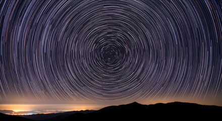 Fototapeta premium Mesmerizing Celestial Dance A Captivating Long Exposure View of Star Trails Arching Across the Night Sky Above Silhouetted Mountains