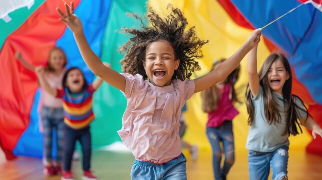 Children play energetically under a colorful parachute canopy during an active indoor group activity.