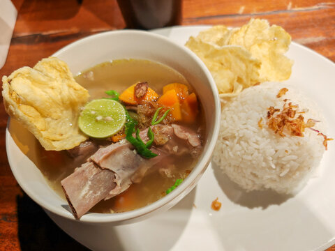Indonesian beef rib soup or sop iga served hot with white rice, lime, and emping crackers