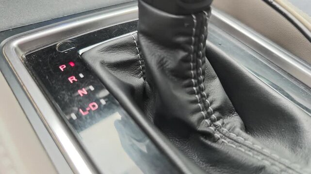 Close up view of a driver changing the gear in an automatic transmission car. The selector lever moves from park through reverse to drive
