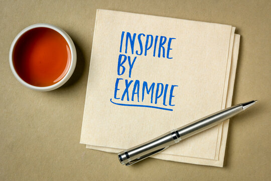 Inspire by Example - inspirational handwritten note on a napkin with tea and pen, encouraging leadership, integrity, positive influence, and personal growth.