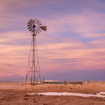 windmill with a pump and cattle water tank in shortgrass prairie, Pawnee National Grassland in northern Colorado, winter or early spring scenery