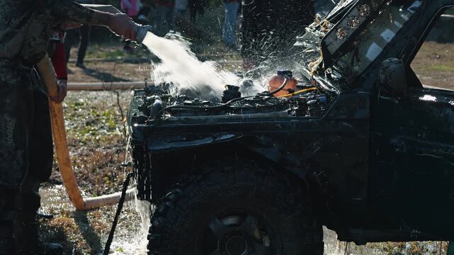 Man in dirty clothes cleans mud from off road vehicle's engine compartment with powerful stream of water. Action shot after extreme mud racing competition. Gritty, dynamic scene