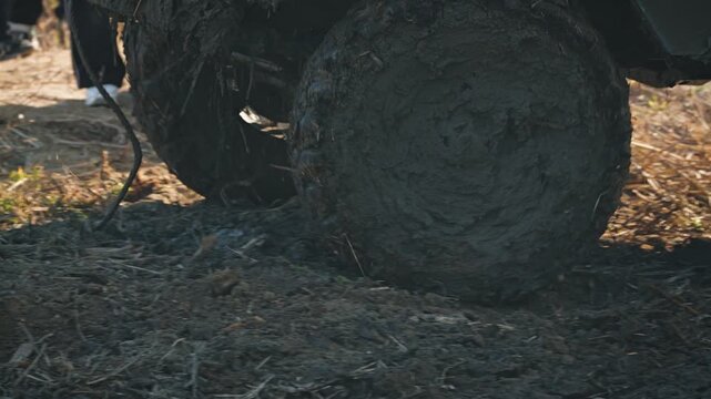 Low angle close up of muddy off road vehicle tires spinning with motion blur during extreme motorsports competition. Dirty wheels churn dirt under bright daylight, conveying power and speed