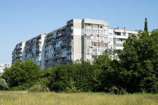 Soviet-era apartment block surrounded by green trees under a clear blue sky