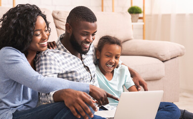 Fototapeta premium Joyful african american family of three using laptop at home together, watching movie or browsing internet