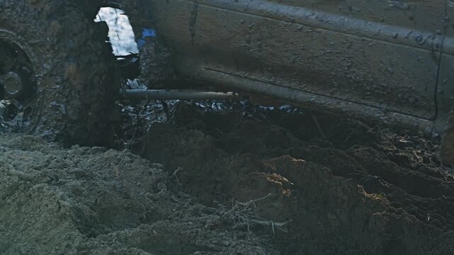 Close up shot SUV wheel covered in thick mud. Vehicle is stuck in deep muddy pit during off road race. Gritty low angle view with monochromatic brown colors captures extreme motorsport action