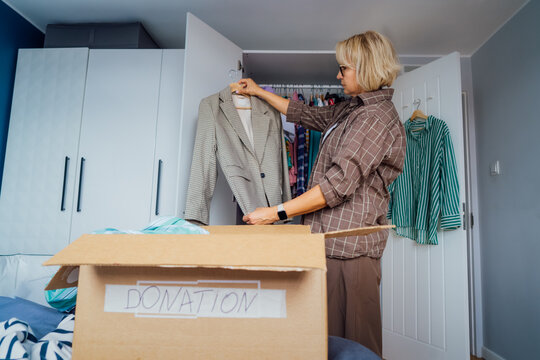 Woman putting selected clothes from her wardrobe for donating to a Charity shop. Decluttering, Sorting clothes and Cleaning Up. Reuse, second-hand concept. Conscious consumer, sustainable lifestyle