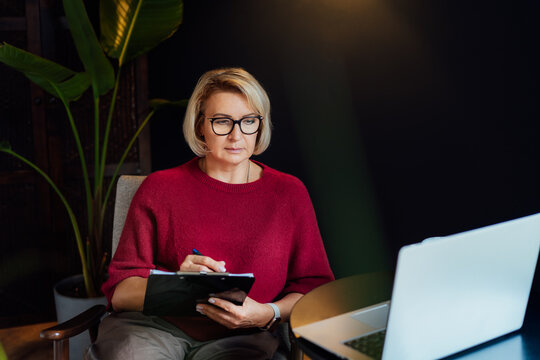 Concentrated 50's stylish, confident mature businesswoman, middle aged experienced senior female professional, business coach, mentor, therapist, counselor working on laptop in office. Female leader