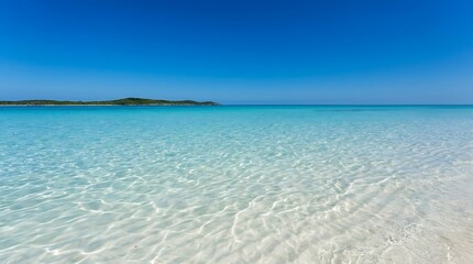 Fototapeta premium Clear blue ocean water at a tropical beach with white sand and a small island on the horizon under a bright sunny sky