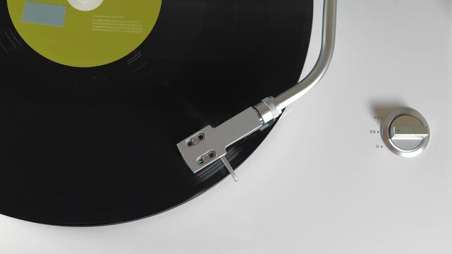 Turntable playing vinyl with stylus tracking LP groove, analog audio playback, hi-fi music equipment, smooth rotation, minimal white background, top view.