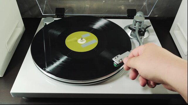 Hands placing vinyl on turntable, lowering stylus onto LP groove and starting analog playback, authentic music listening experience, audiophile equipment.
