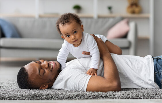 Adorable Cute Baby Boy Lying On Father's Chest While They Relaxing At Home Together, Happy African American Dad Spending Time With His Infant Child, Enjoying Paternity Leave, Closeup